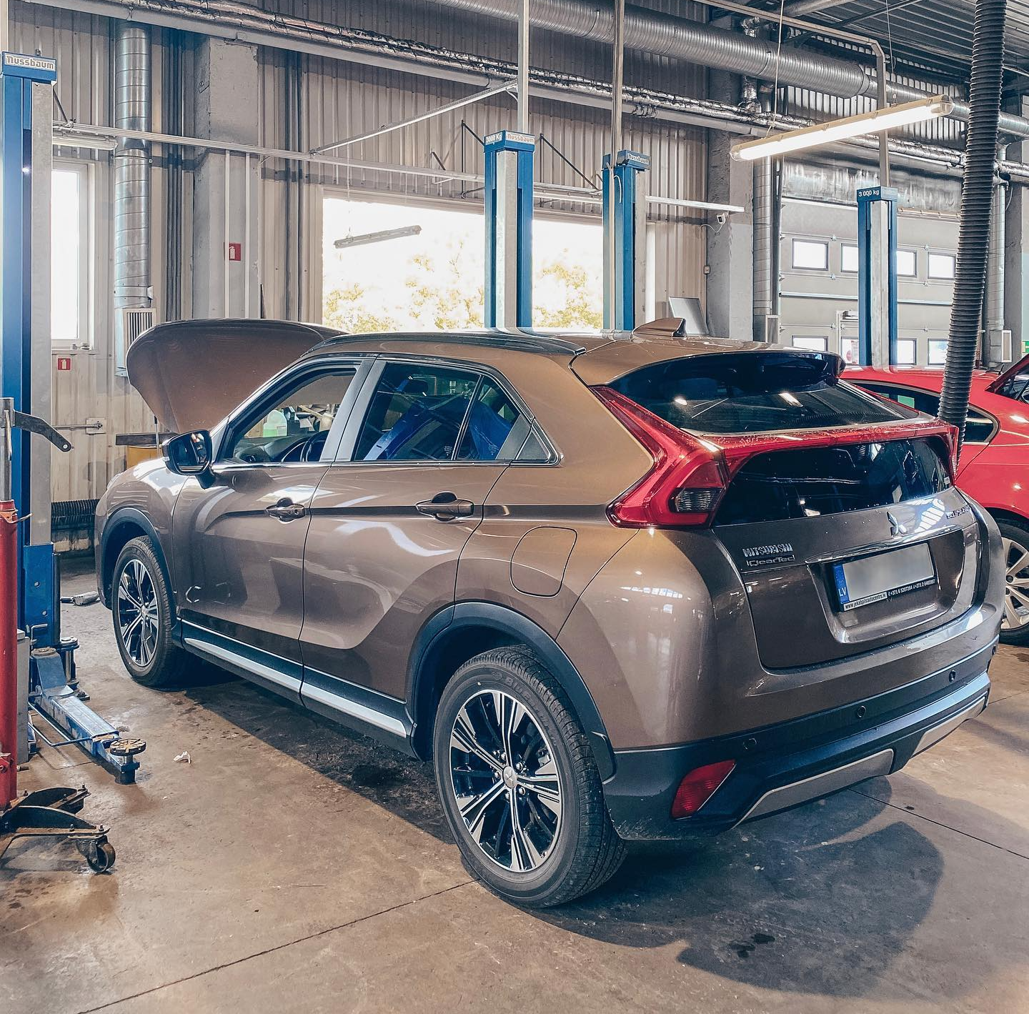 Auto ar uzvilktu motora pārsegu sēž garāžā uz pacēlāja.