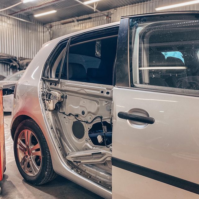 Sudraba auto ar atvērtām durvīm garāžā.