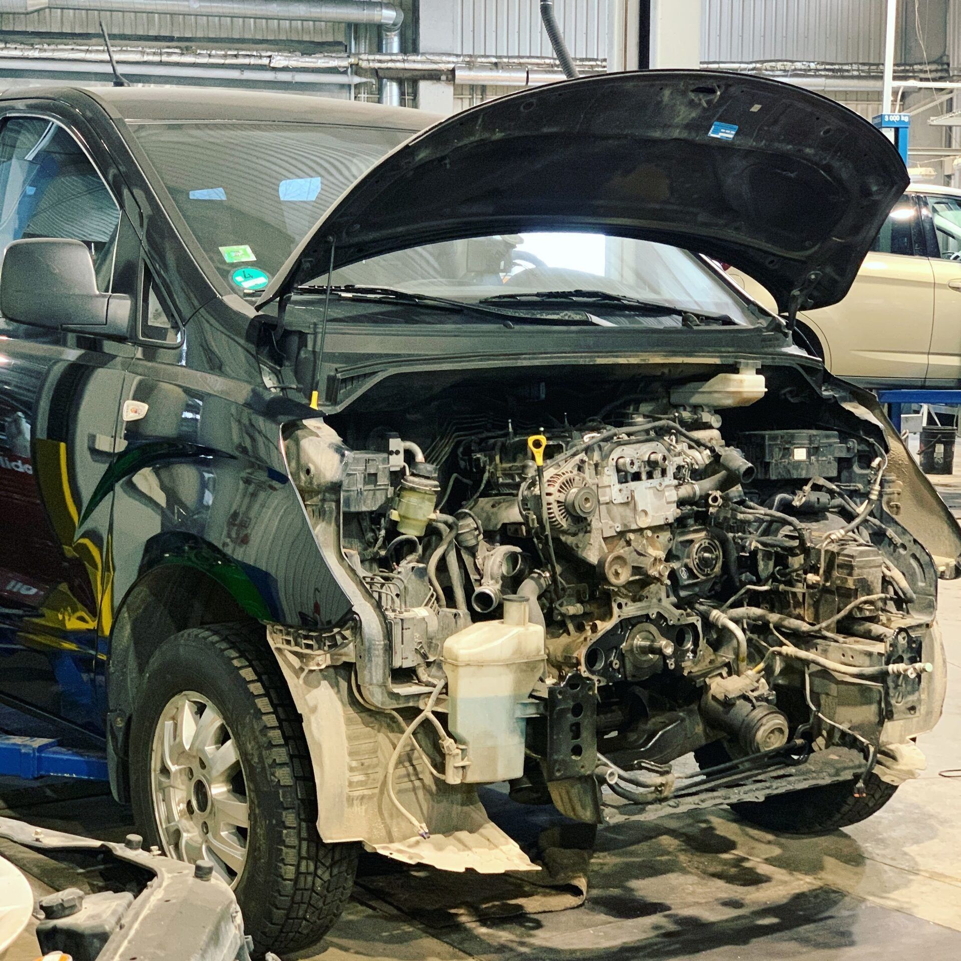 Automašīna ar atvērtu motora pārsegu sēž garāžā.