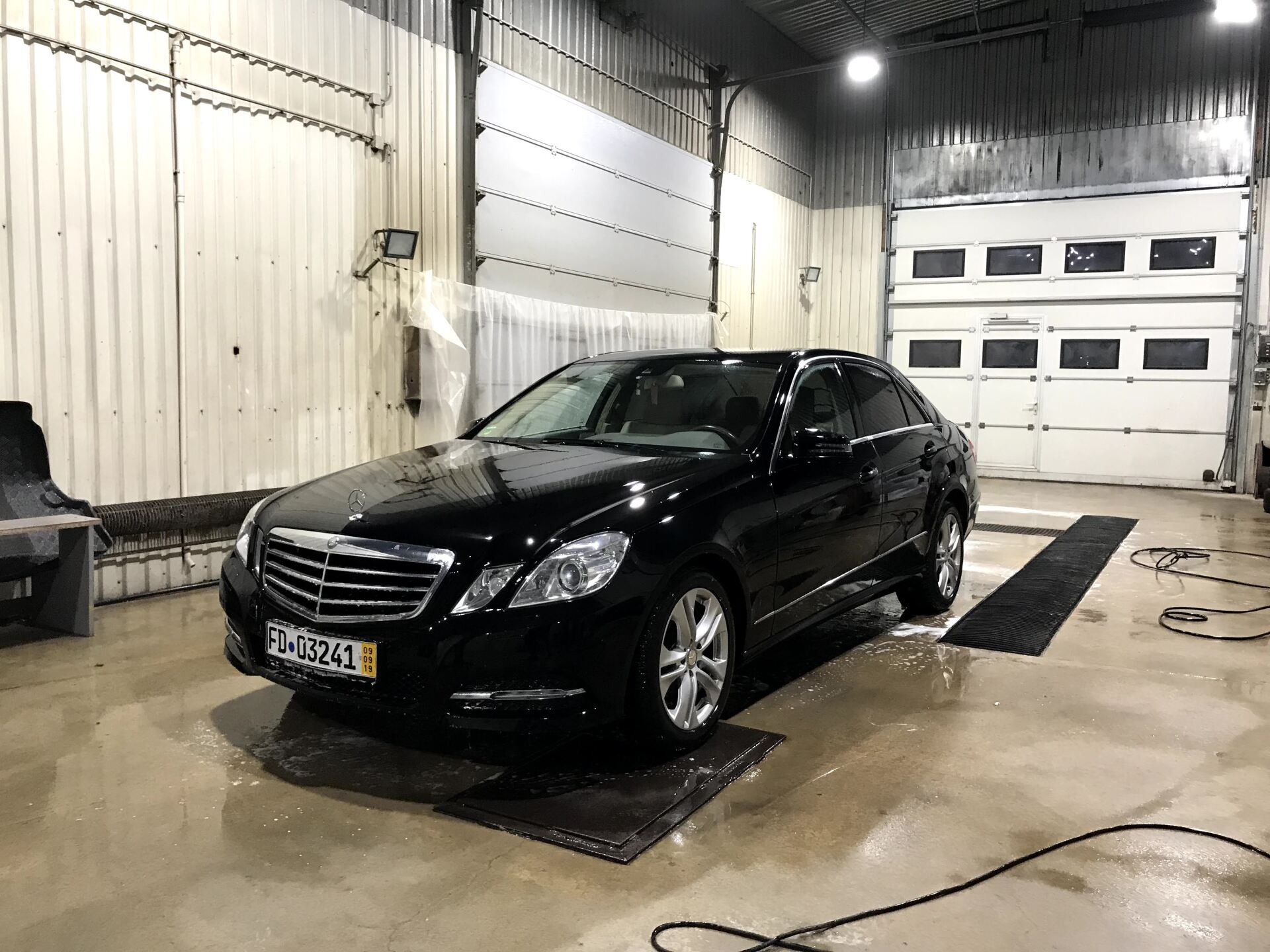 Melna mašīna stāv garāžā pie garāžas durvīm.