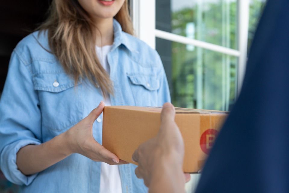 Happy smiling woman receives boxes parcel from courier in front house. Delivery man send deliver express. online shopping, paper containers, takeaway, postman, delivery service, packages