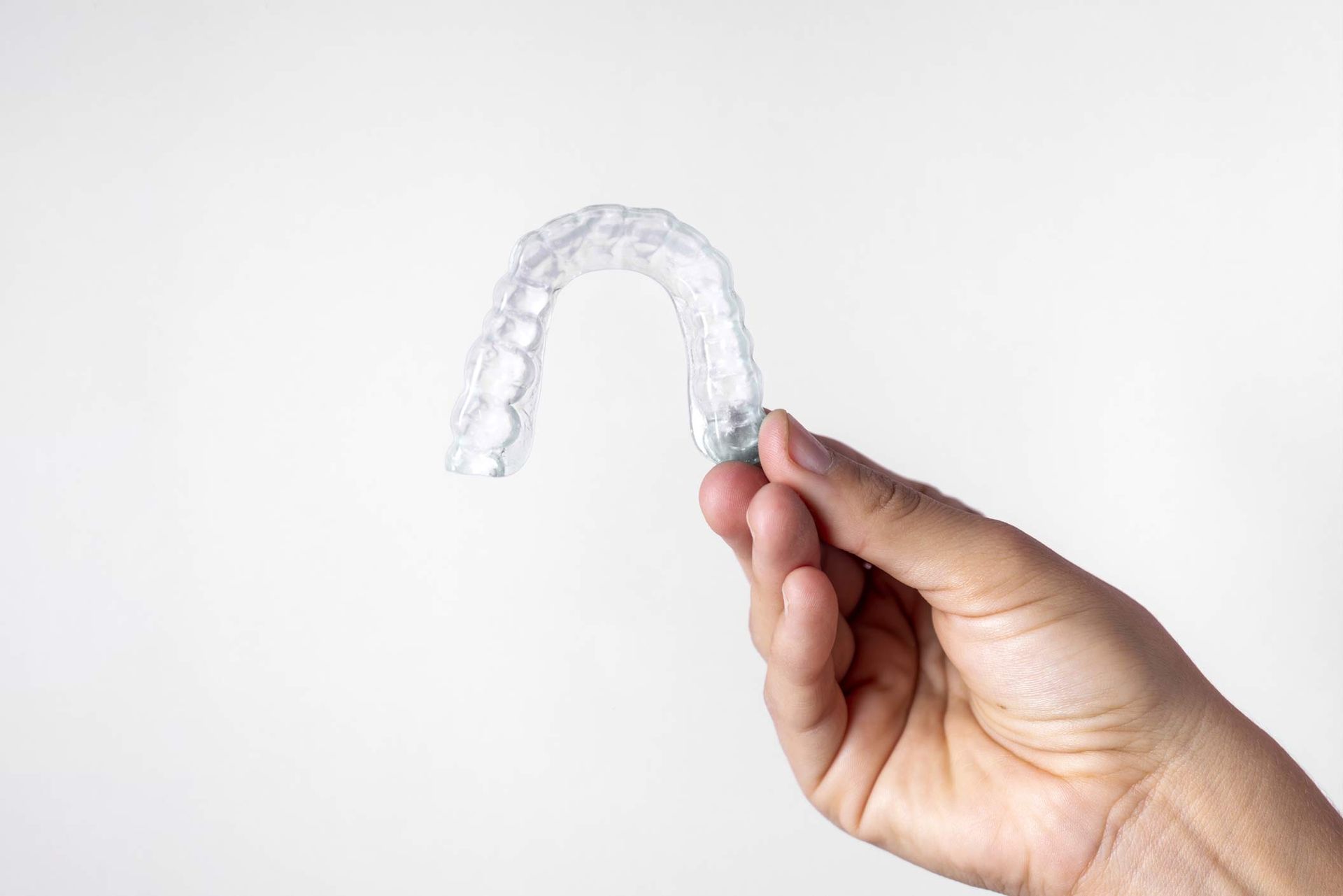 Hand holding a clear dental aligner against a plain white background.