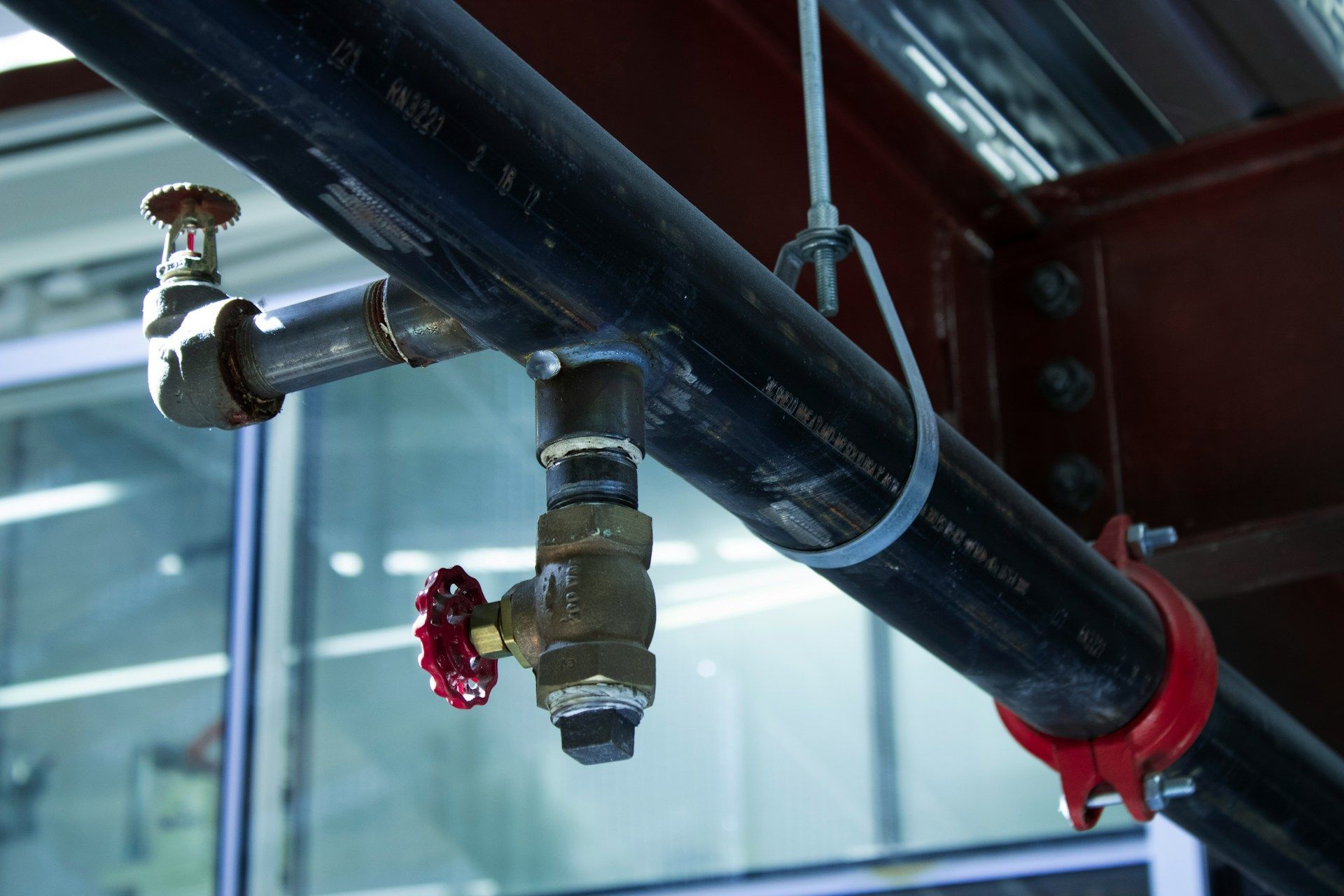 Close-up of industrial pipes with red valve handles and a sprinkler head on a ceiling.
