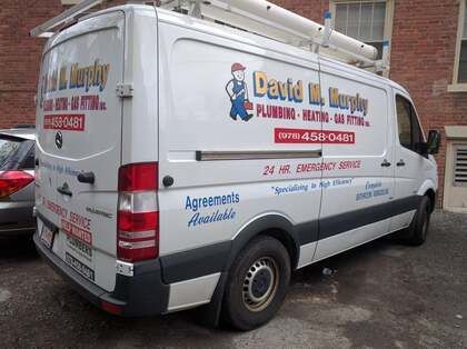 White plumbing service van parked outdoors, with company branding and contact details on the side.