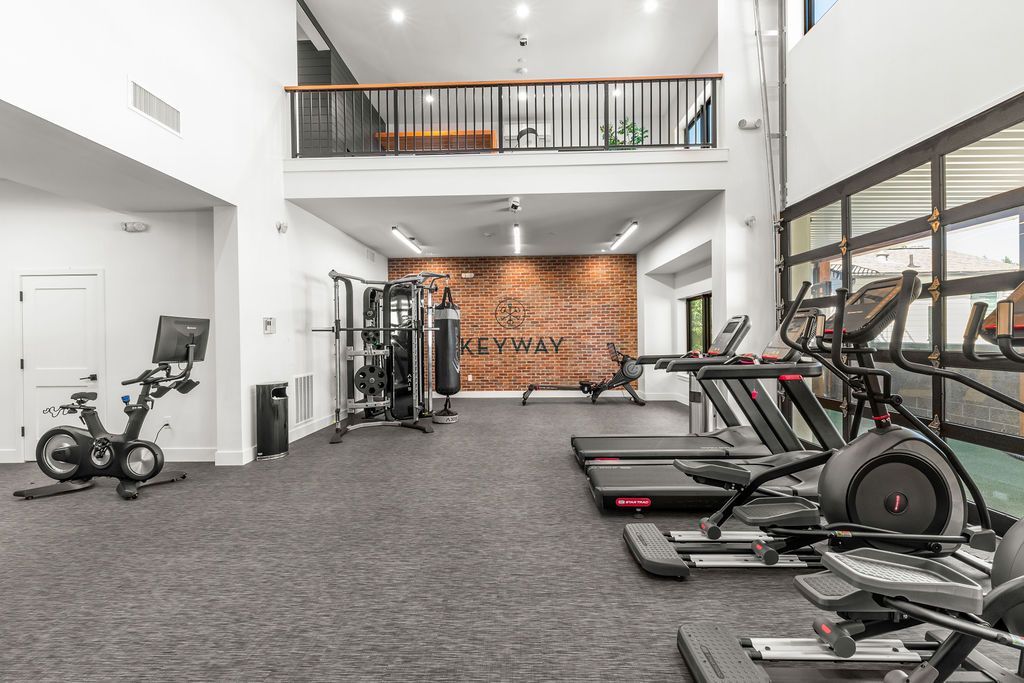 Gym interior with exercise equipment: treadmills, bikes, weights, punching bag, and a loft area.