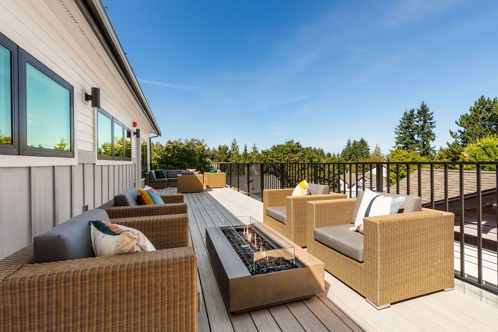 Outdoor deck with wicker furniture, fire pit, and wooden railing, on a sunny day.
