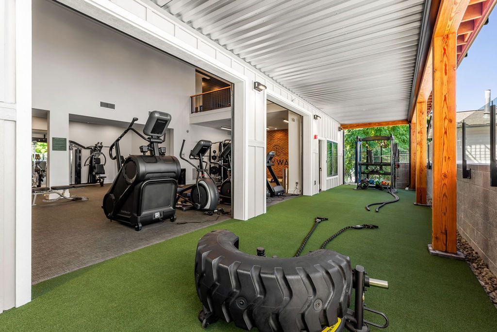 Gym with exercise equipment, green turf floor, and a tire. Outdoor setting with bright light.