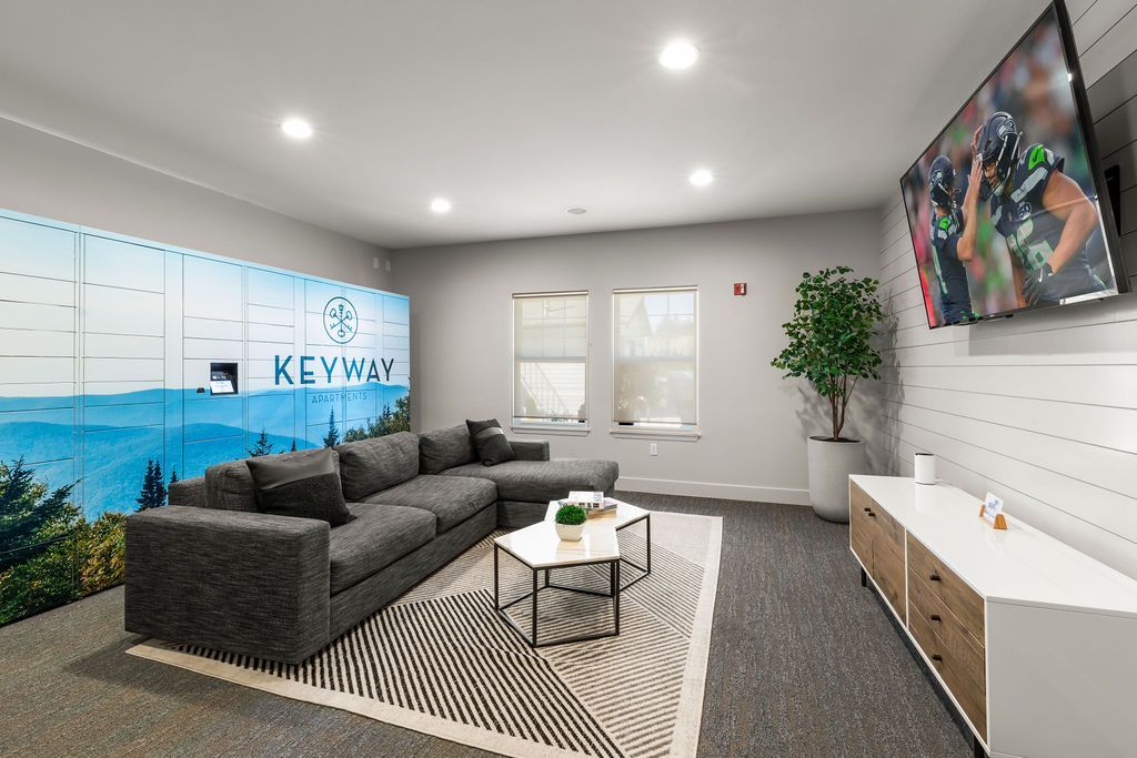 Lounge area with a gray sectional, TV, lockers, coffee table, and large windows.