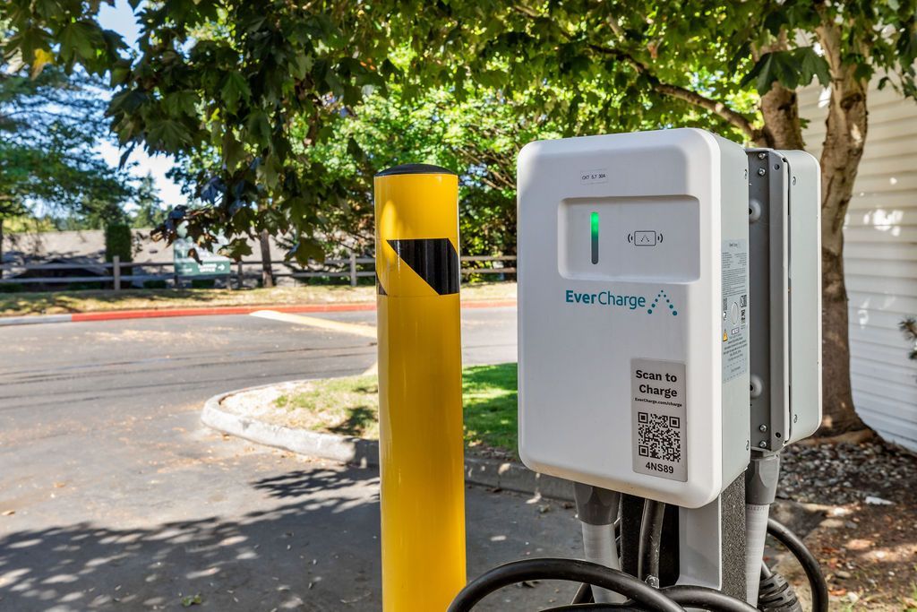 An electric vehicle charging station with a green status light, next to a yellow bollard.