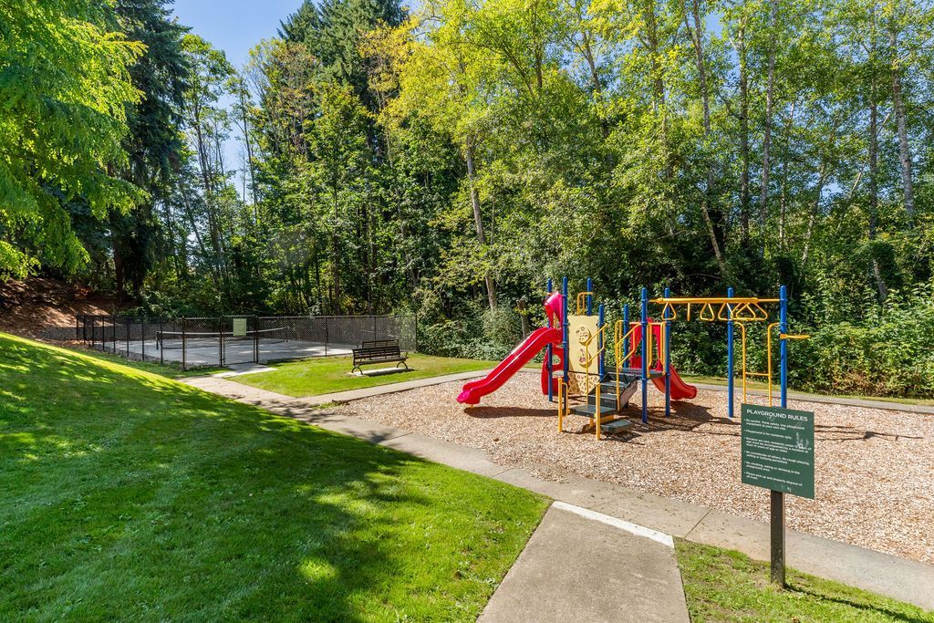 Playground with red slide, swing set, and wood-chip ground covering surrounded by trees.