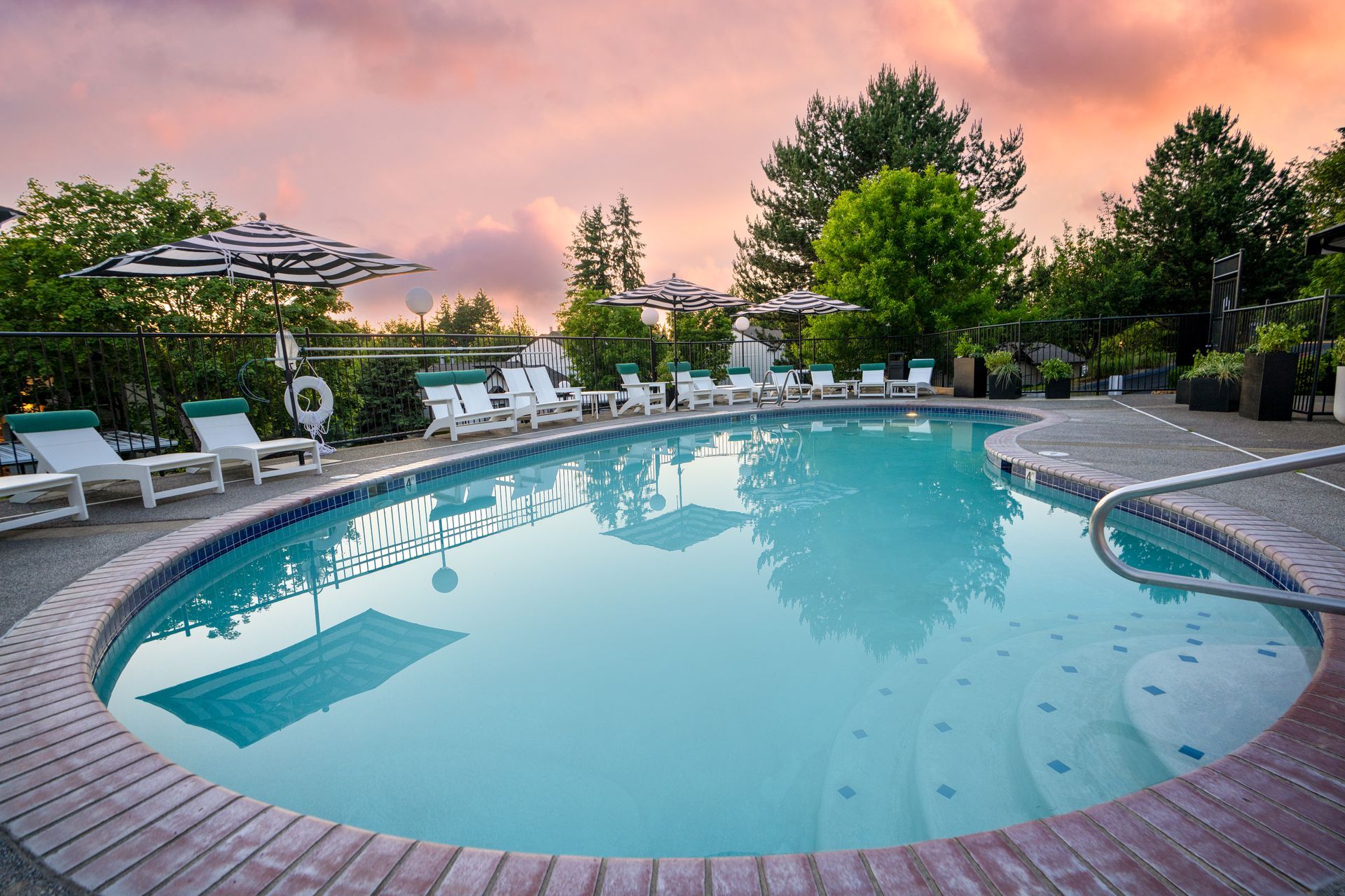 Swimming pool with lounge chairs, under a sunset sky.