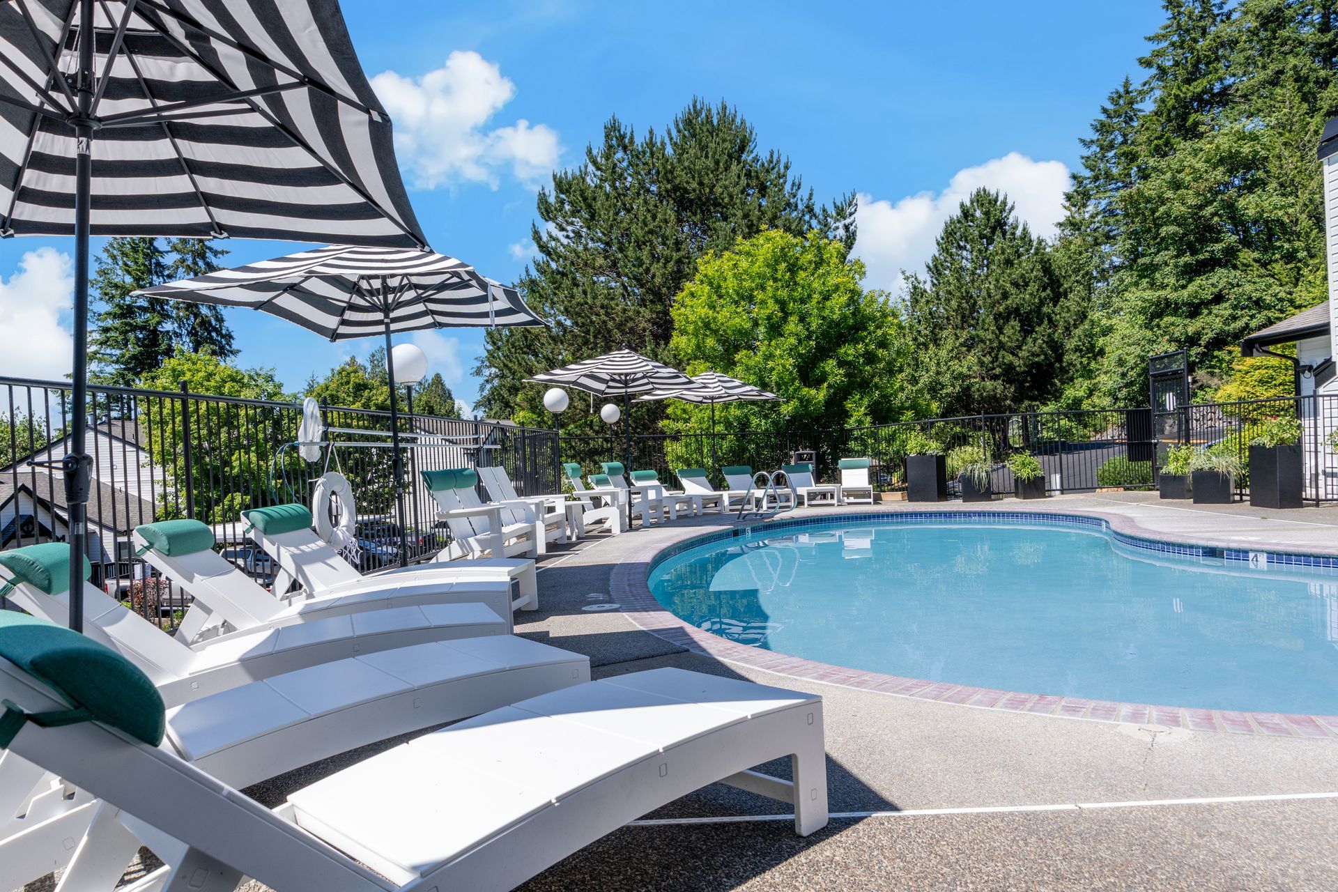 Pool with lounge chairs and striped umbrellas, surrounded by trees and greenery.