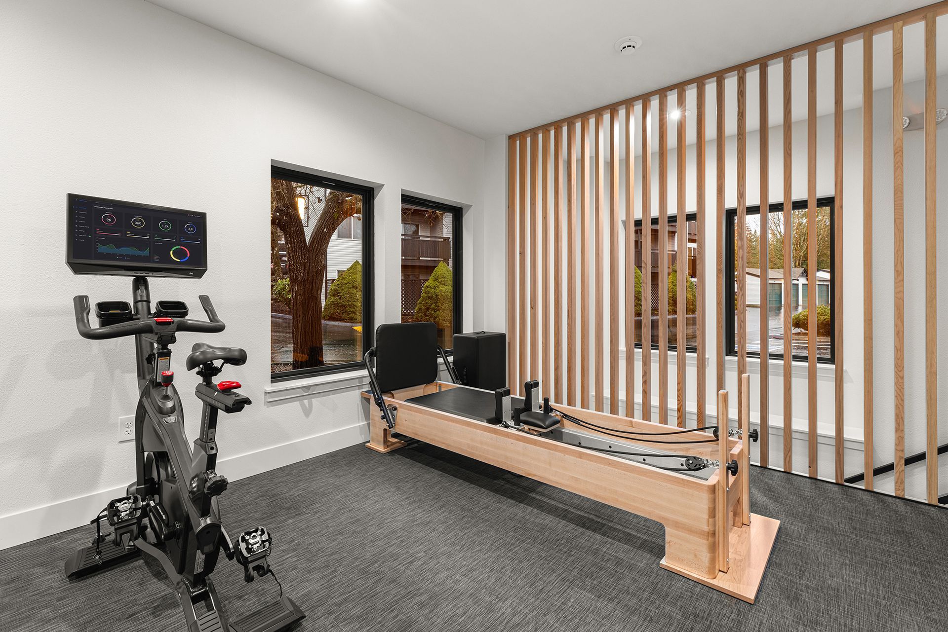 Home gym with Peloton bike, rowing machine, windows, and wood slat partition.