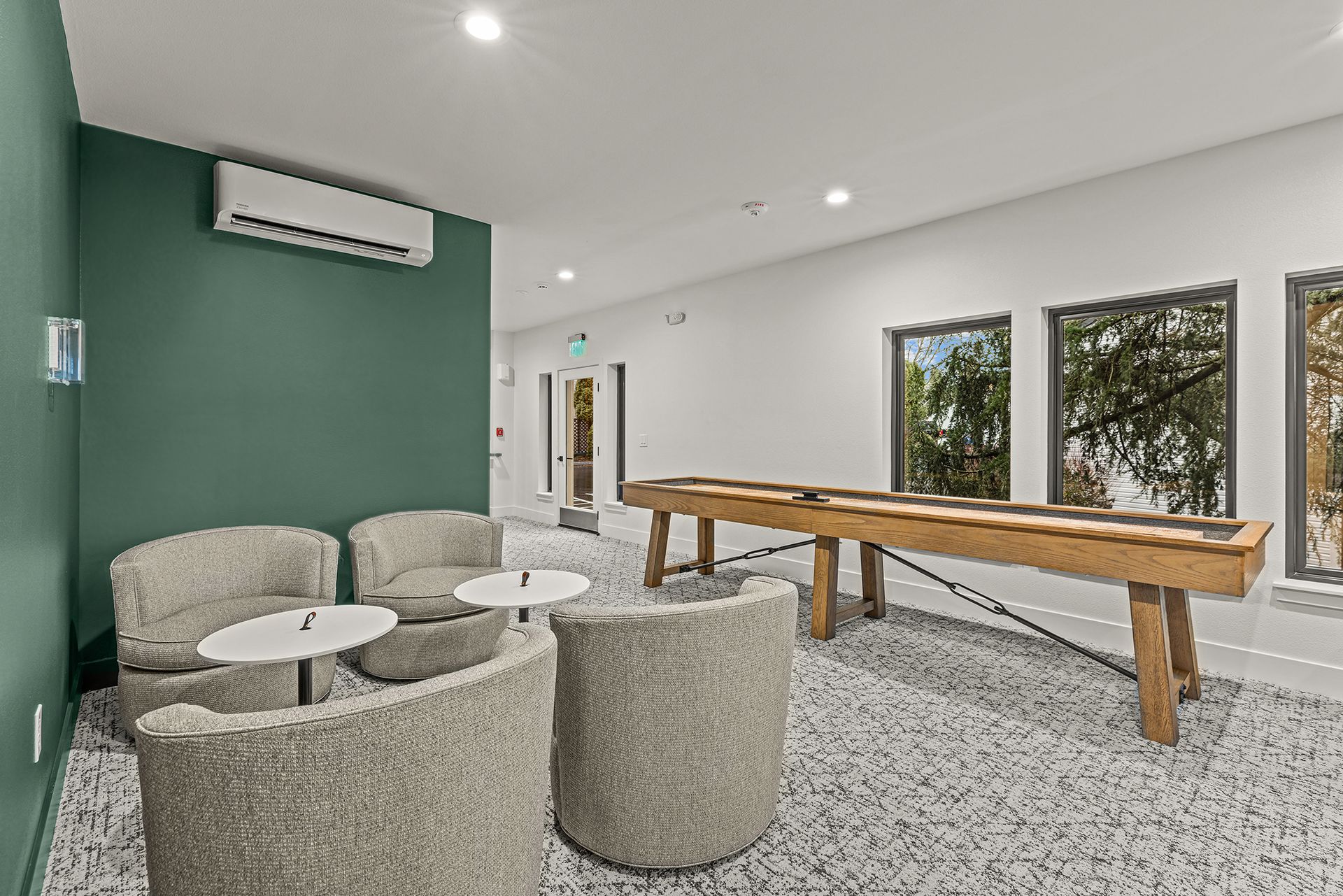 Cozy lounge with shuffleboard, green wall, comfortable chairs, and windows.
