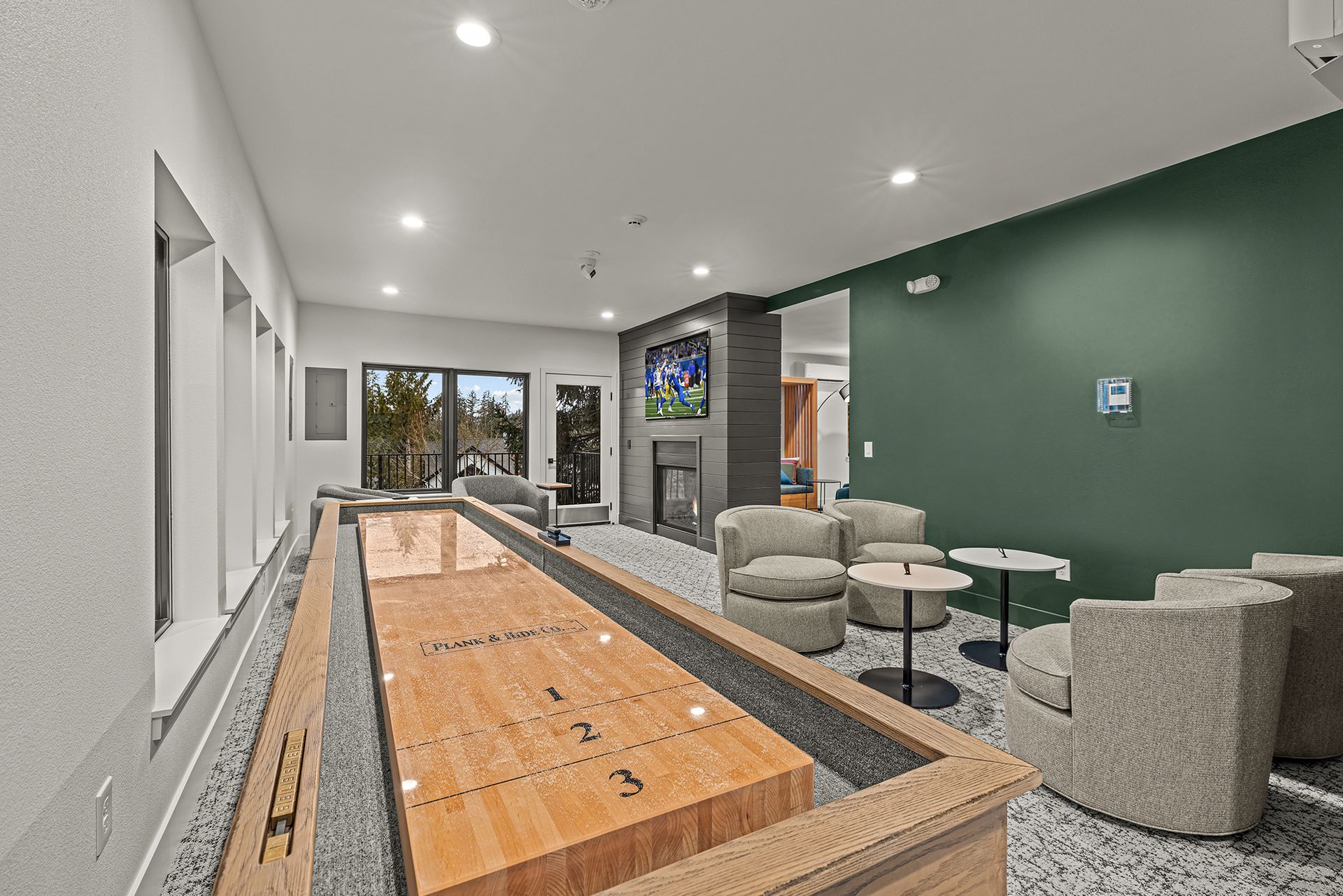 Shuffleboard in a modern lounge with green accent wall, seating area, and fireplace.
