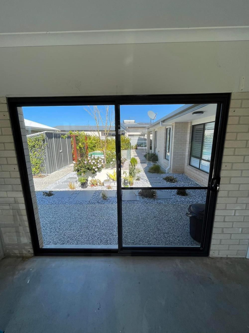 A Sliding Glass Door With A View Of A Garden And A House — Eastcoast Aluminium & Glass In Ballina, NSW