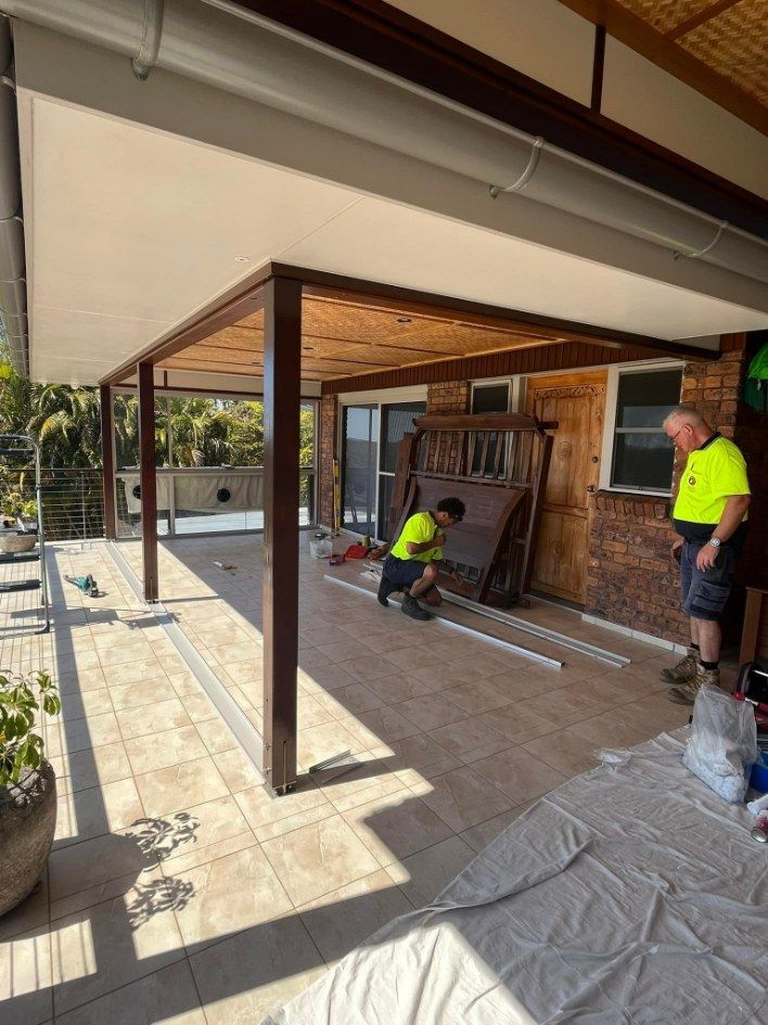 Two Workers in a Covered Patio Are Installing Framing — Eastcoast Aluminium & Glass In Ballina, NSW