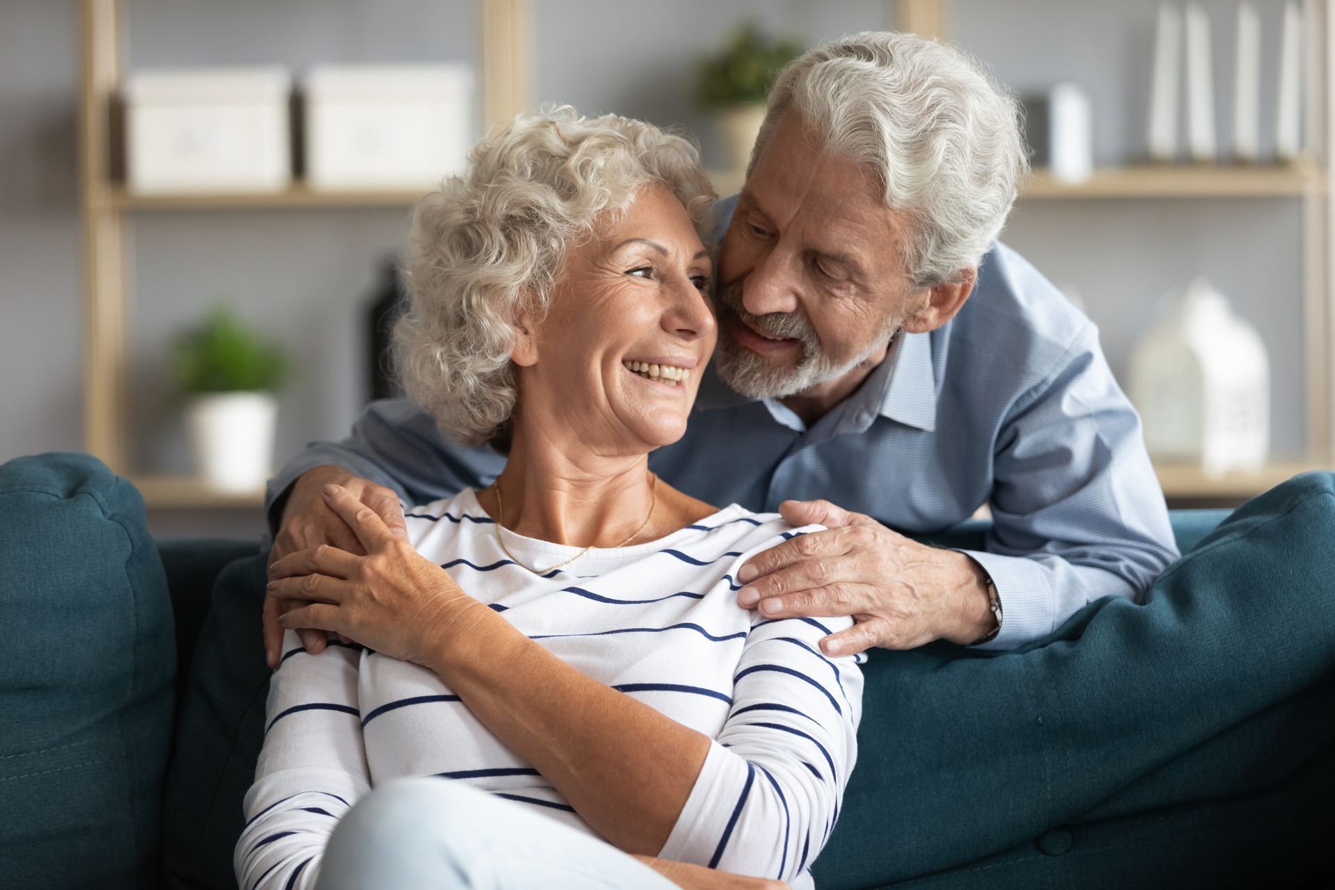 An elderly couple is sitting on a couch and hugging each other.