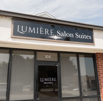 an image of the store front that B. Glam Beauty Salon is inside of. There is a black sign that says Lumiere Salon Suites with glass windows and doors