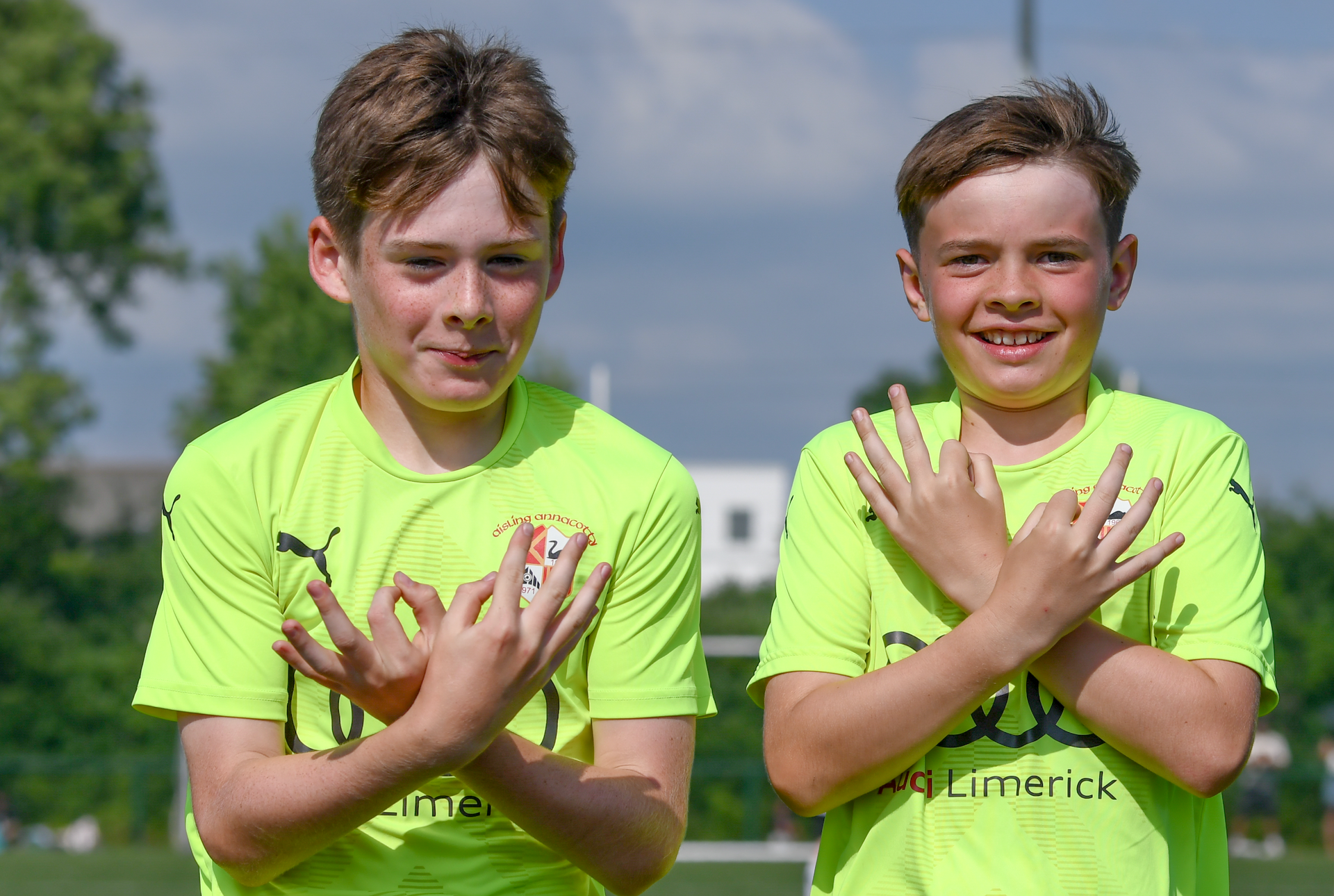 Two young boys in neon green shirts are standing next to each other on a field.