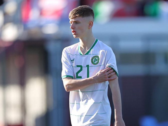A young man wearing a white and green soccer jersey with the number 21 on it.