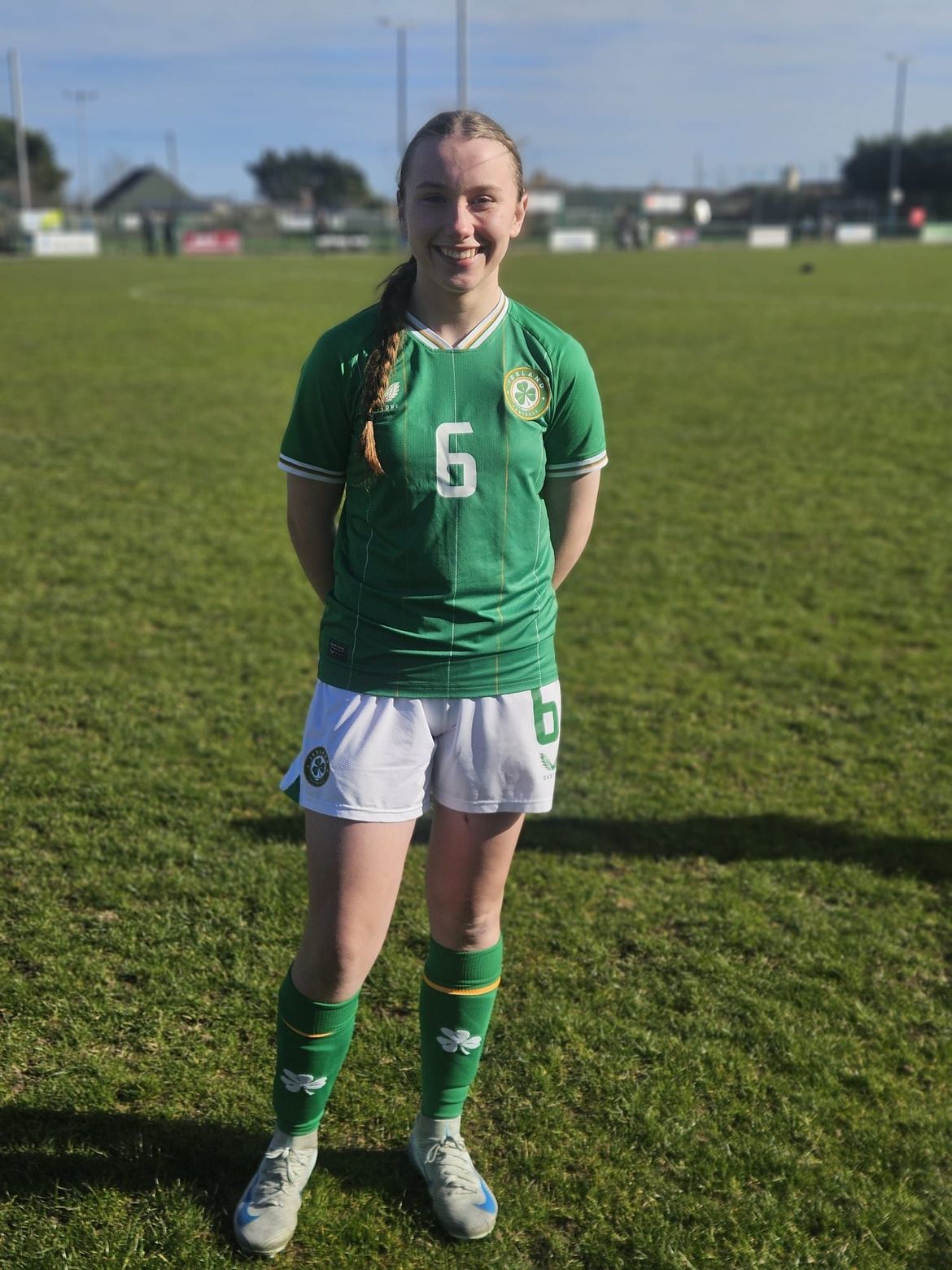 A young girl in a green soccer uniform is standing on a field.