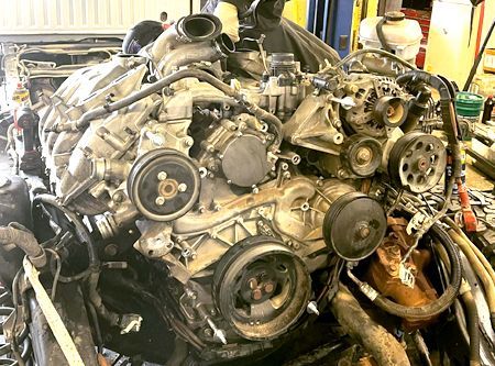 Engine with pulleys and belts, possibly disassembled in a garage.