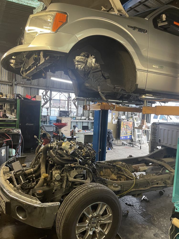 Silver pickup truck lifted, engine removed, in a repair shop.