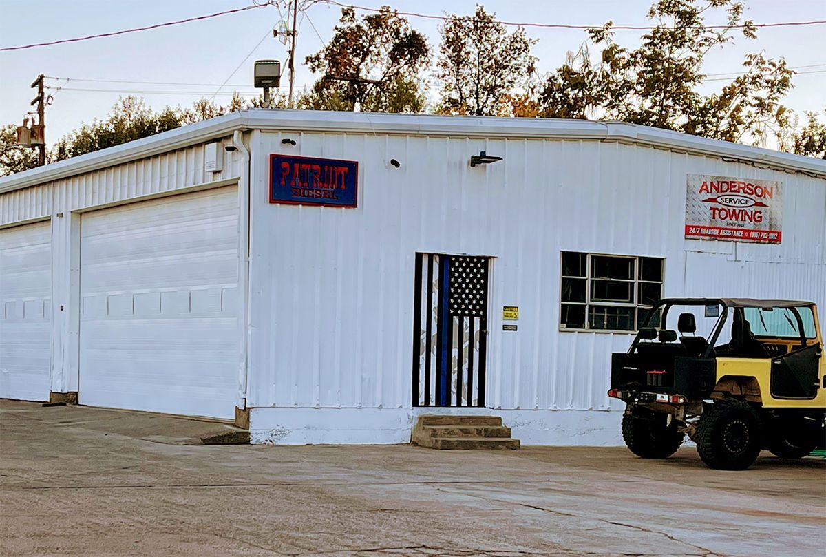 White building with garage doors and a yellow Jeep; US flag hangs over the door.