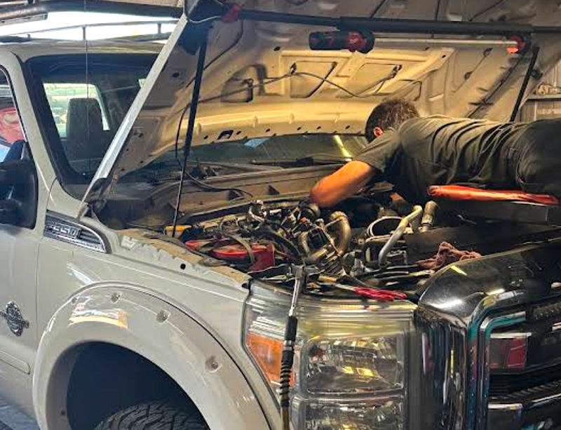 Mechanic working on a white truck with the hood open in a shop.