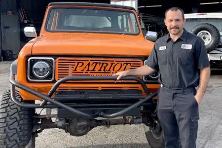 Man in mechanic's uniform beside orange International Scout 