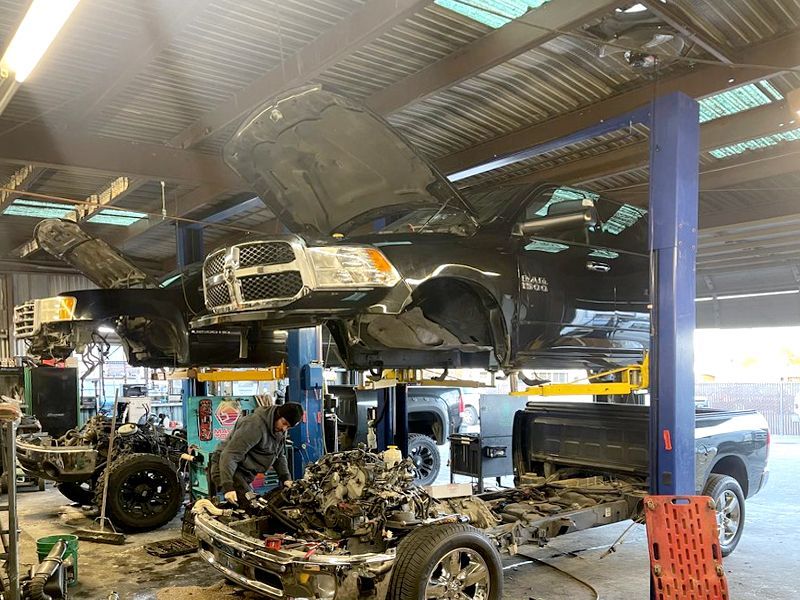 Black pickup truck in auto repair shop being worked on, parts disassembled. Mechanic works on frame.
