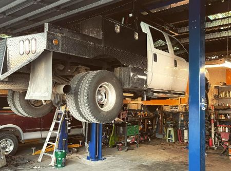 Truck on a lift in a repair shop, showing undercarriage. Two sets of rear tires are visible.