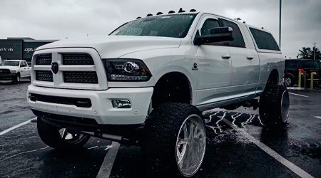 White lifted Dodge Ram truck with large tires parked on wet pavement.