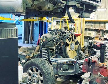 Truck chassis with engine exposed in repair shop, undercarriage visible.