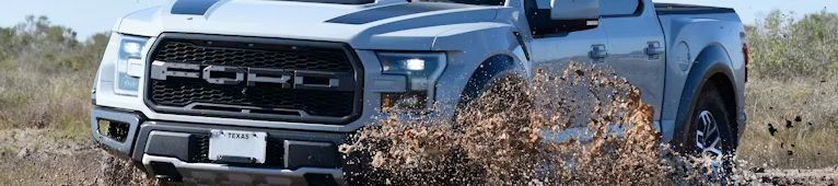 Gray Ford Raptor truck driving through mud, kicking up a splash.