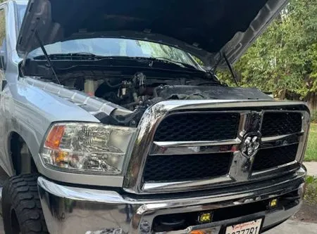 Silver Dodge Ram truck with hood open. Front view of engine compartment and chrome grill.