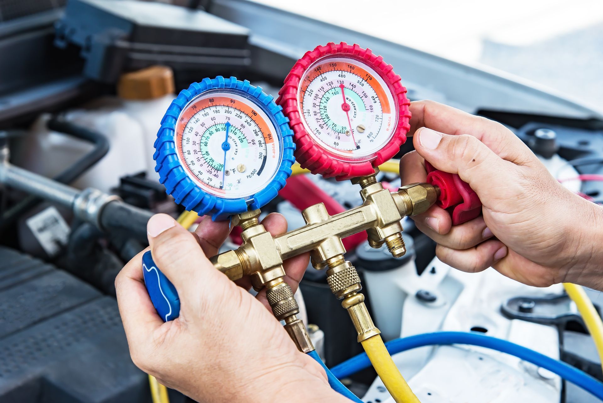 Technician using blue and red manifold gauges to test a car's air conditioning system