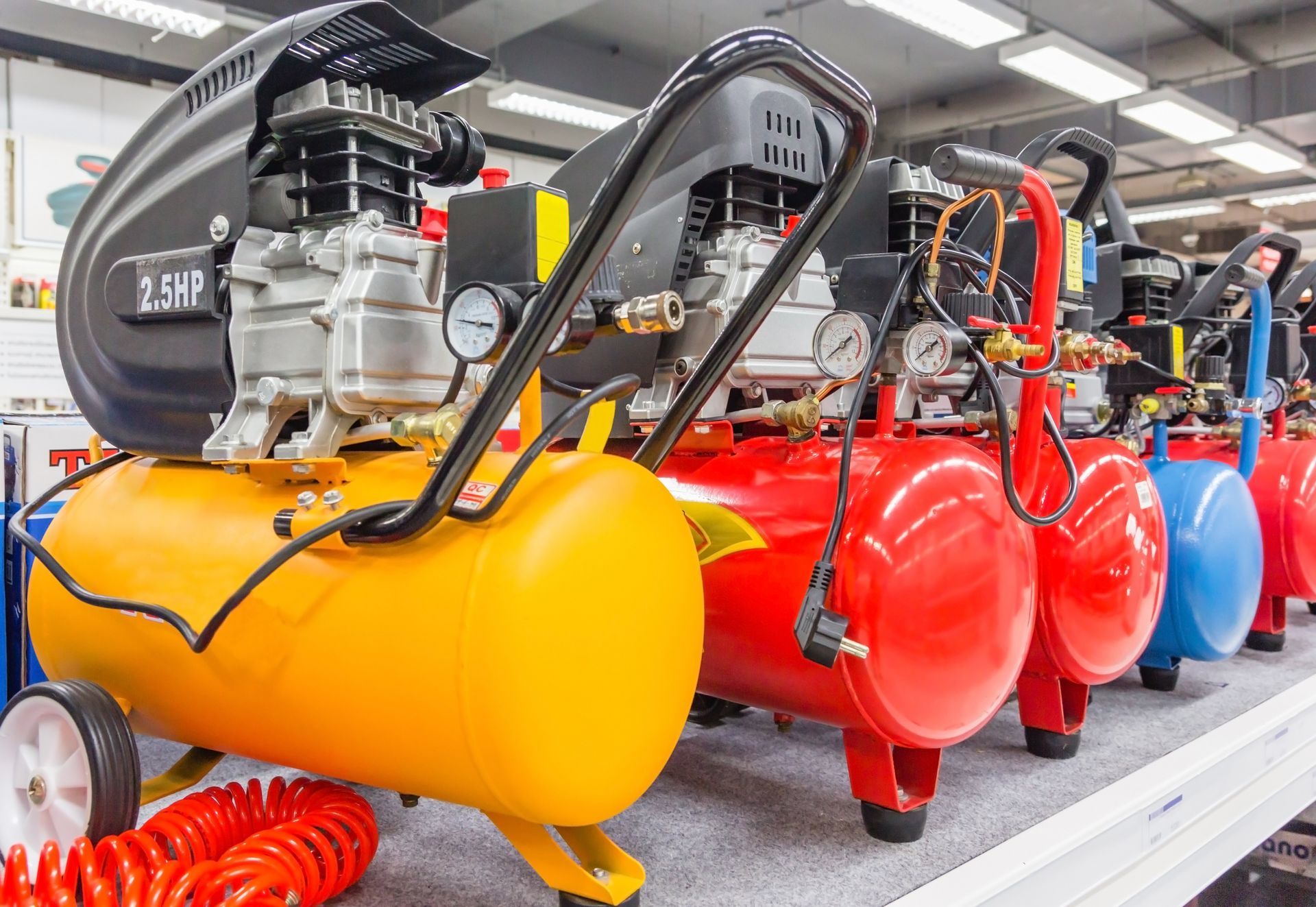 Row of colorful air compressors with tanks and gauges in a store setting.