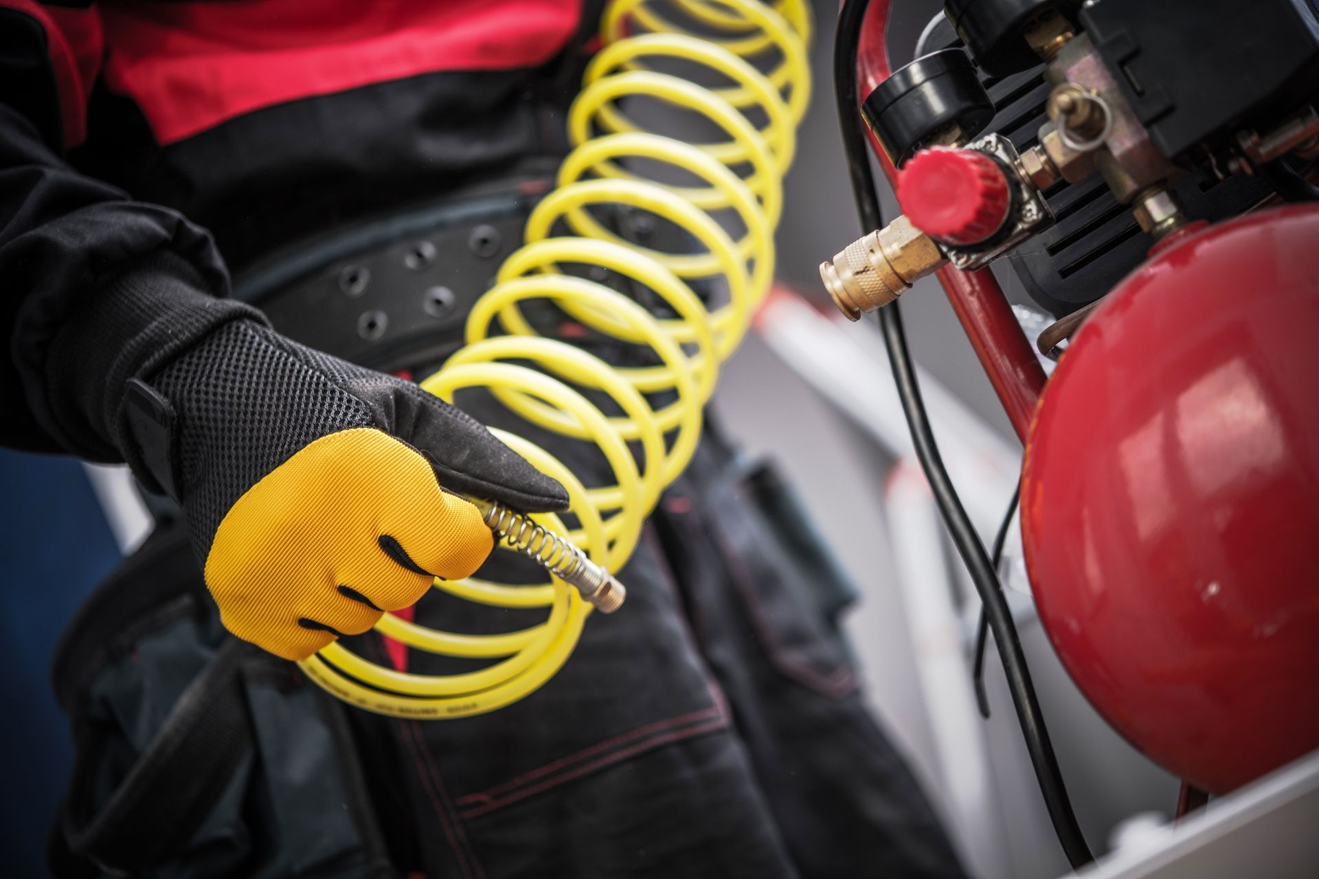 Person in black and red workwear holding yellow air hose, near red air compressor.