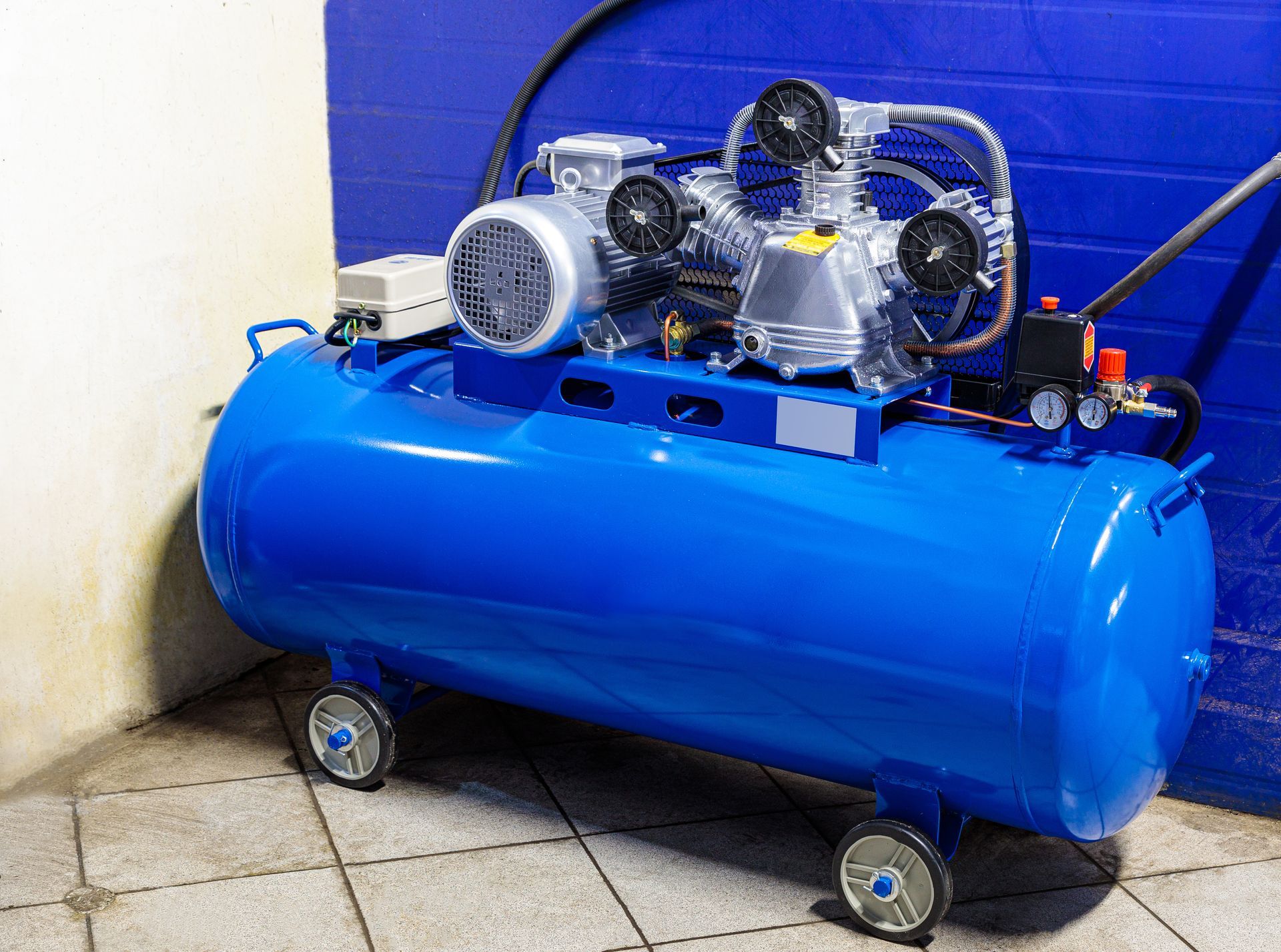 Blue air compressor with wheels in a workshop setting.