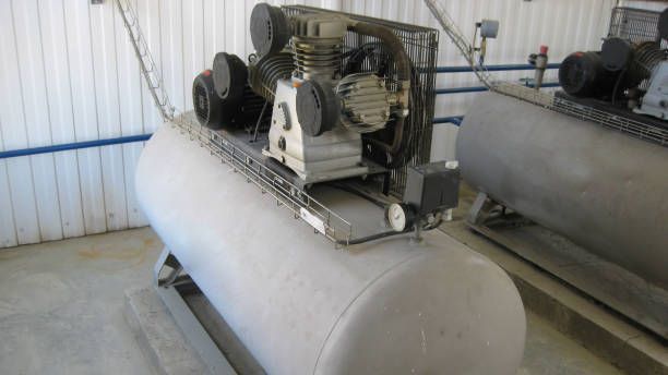 Air compressor with a cylindrical tank, inside an industrial setting.