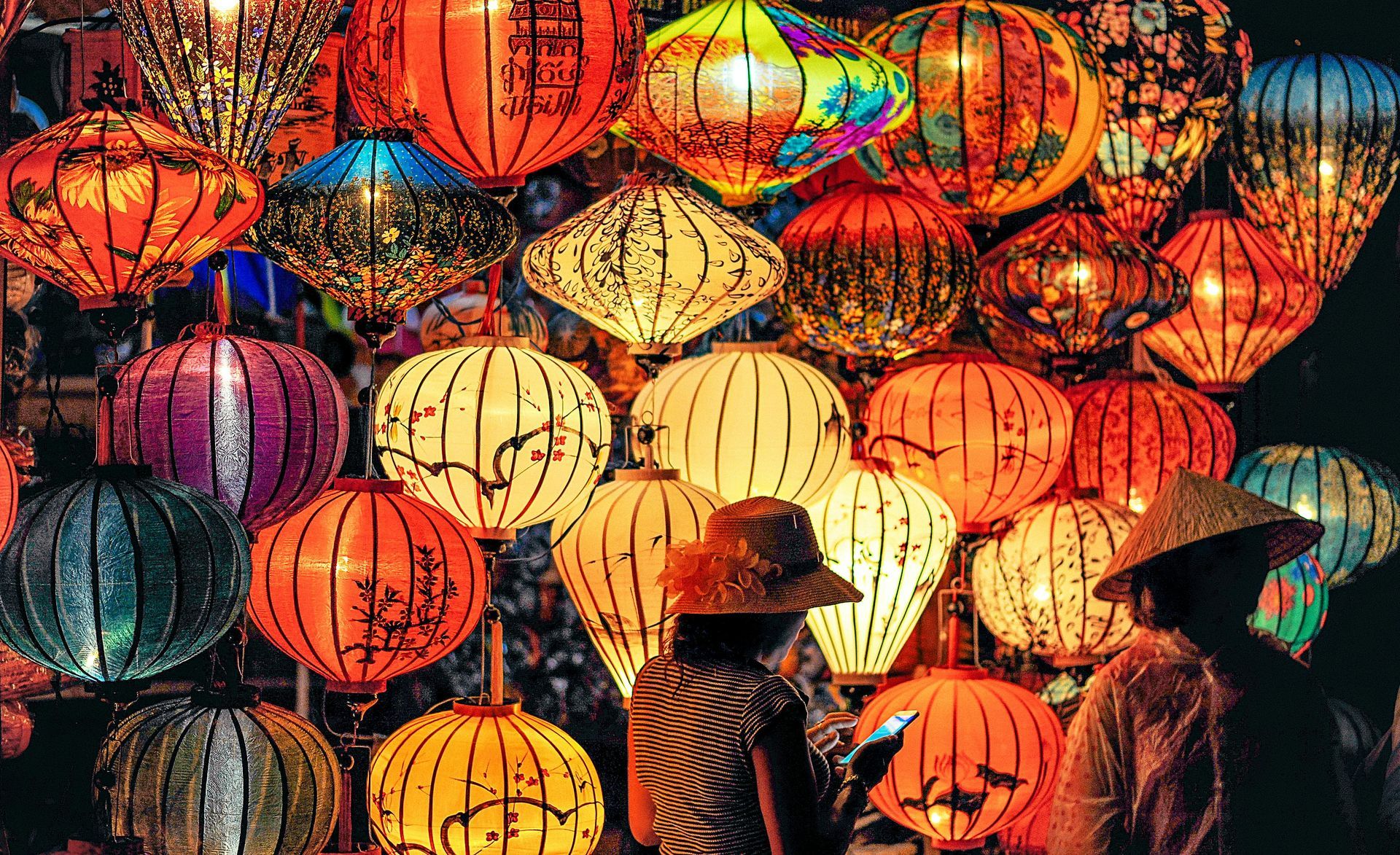 People viewing colorful paper lanterns in a market, with warm, glowing lights.