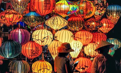 People viewing colorful paper lanterns in a market, with warm, glowing lights.