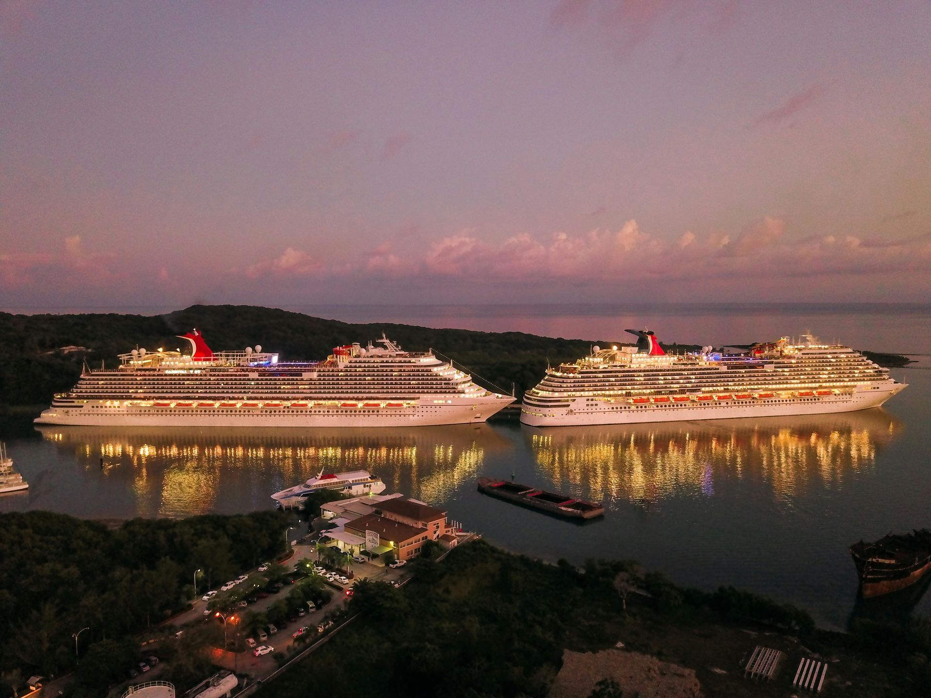 Two cruise ships docked in a bay at dusk with lights reflecting on the water.