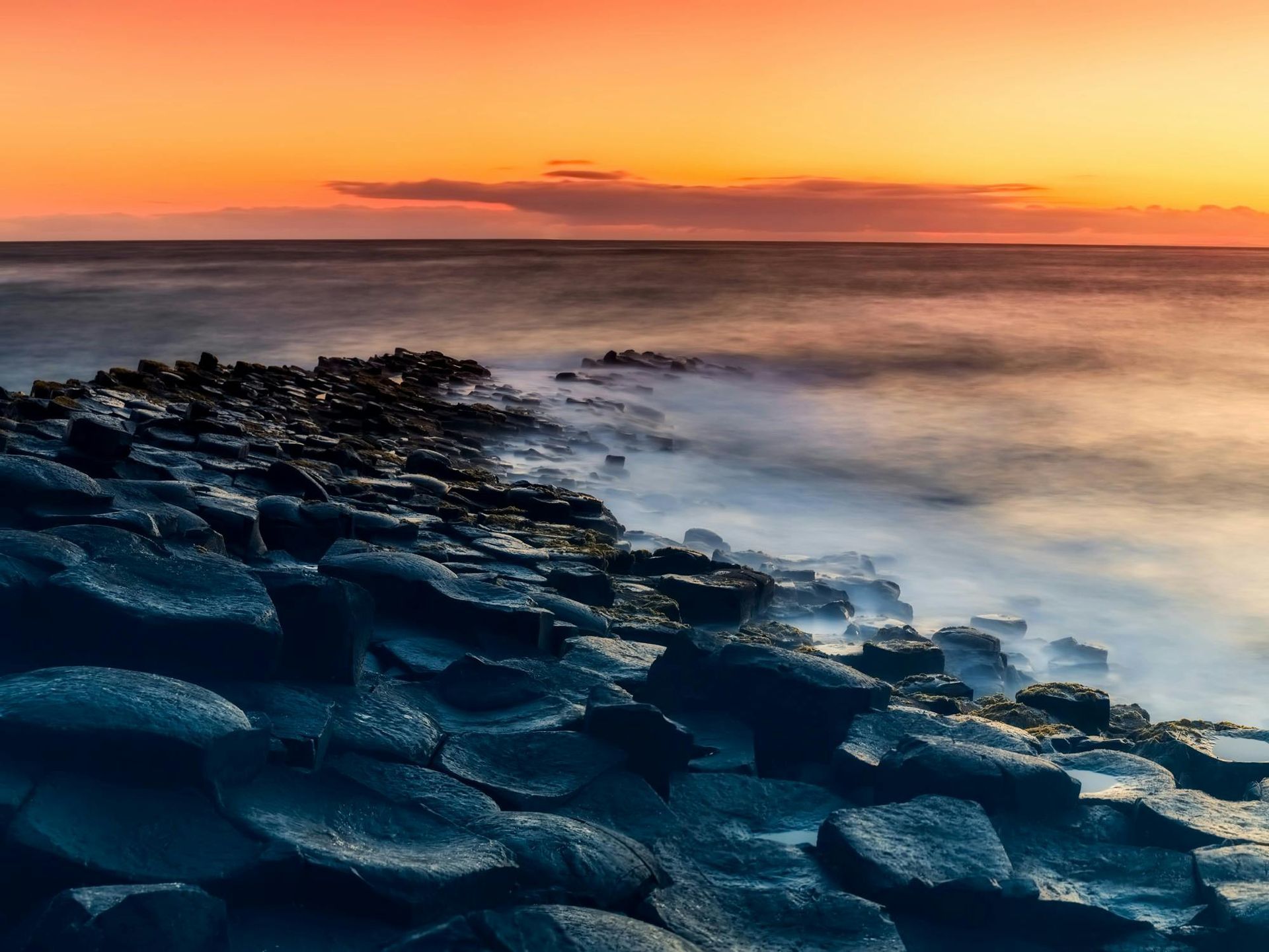 Sunset over dark, hexagonal basalt columns at the Giant's Causeway, Northern Ireland.