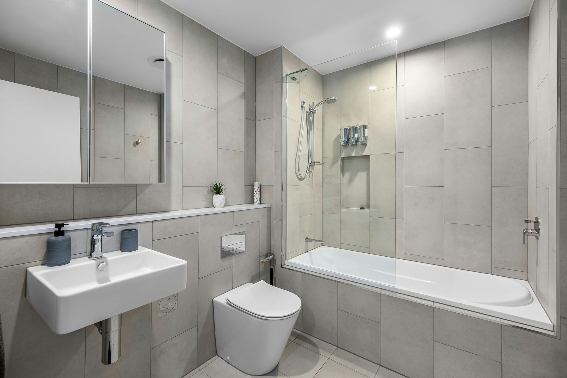 Modern gray bathroom with sink, toilet, mirror, and bathtub shower