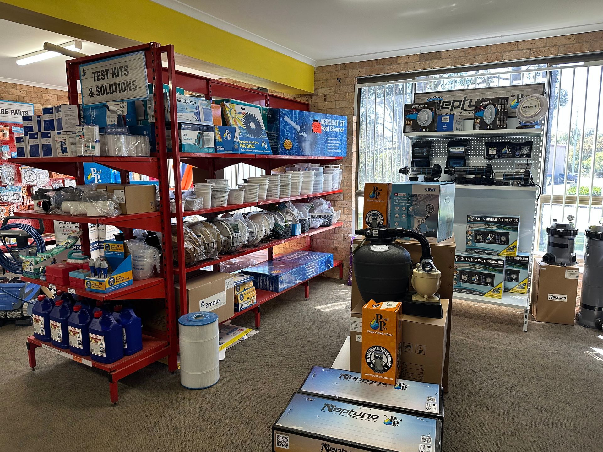 Shelves stocked with pool supplies in a retail store; red shelving, bright interior. — Manning Pools, Rubber & Foam In Taree, NSW