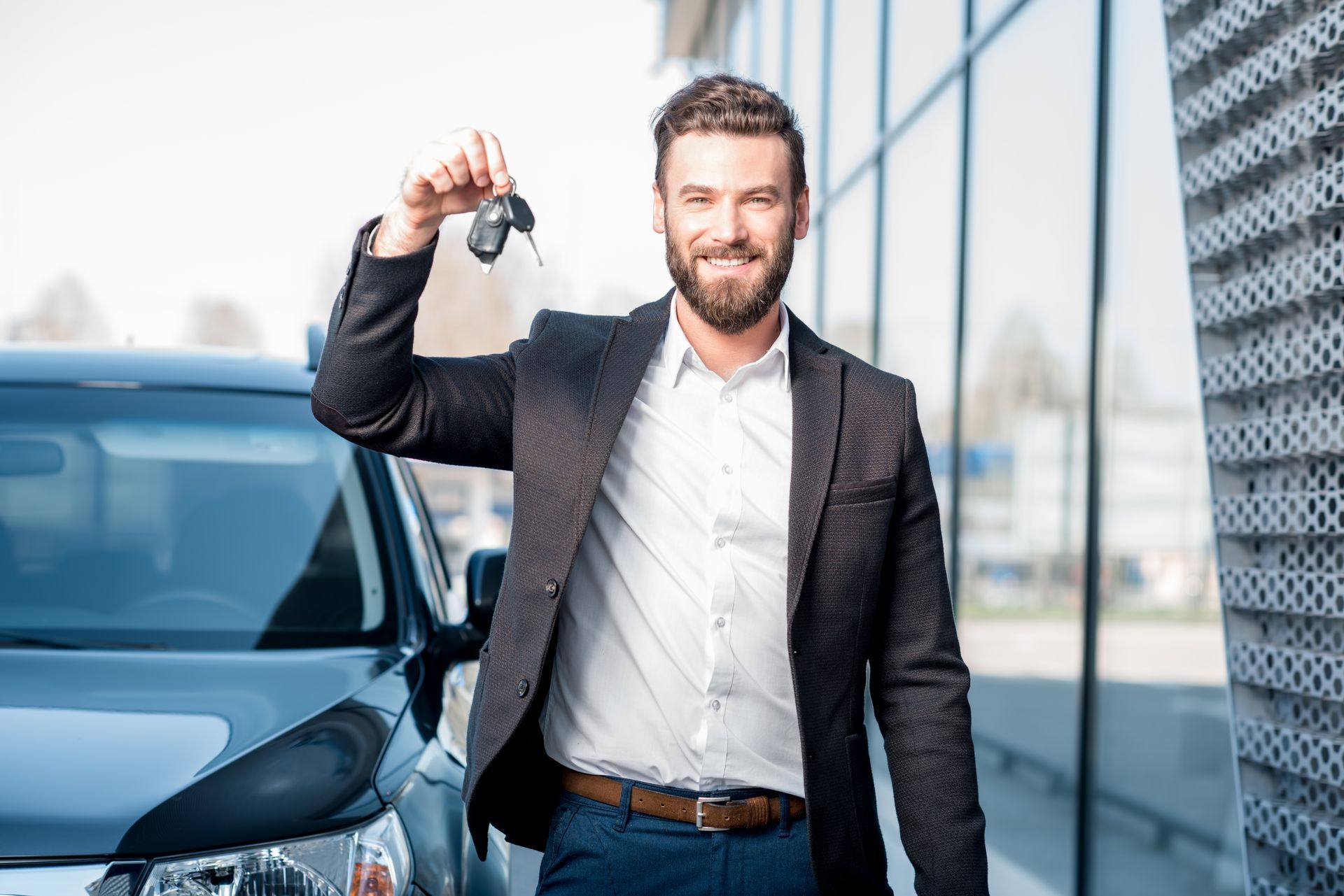 a man in a suit is holding a car key in front of a car