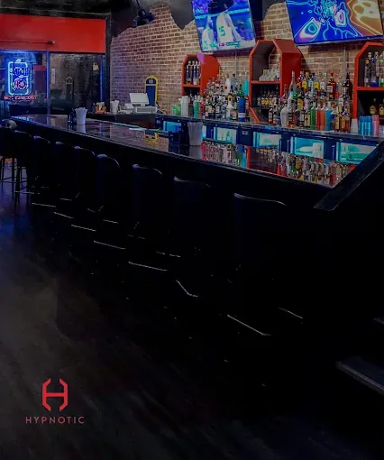 Long black bar with stools, liquor bottles, and TVs. A bar with a brick wall and the logo